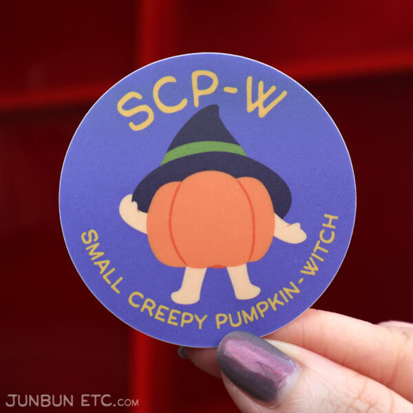 A photo showing a sticker of Small Creepy Pumpkin (SCP), an ambulatory pumpkin with little baby-sized arms and limbs, wearing a witch hat jauntily and holding the brim with one hand. The caption above it says "SCP-W" and below, "Small Creepy Pumpkin-Witch."